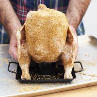 3. Hold the chicken by the wings and lower it onto the rack so that the canister goes into the body cavity. Pull the legs forward so that the chicken stays upright.